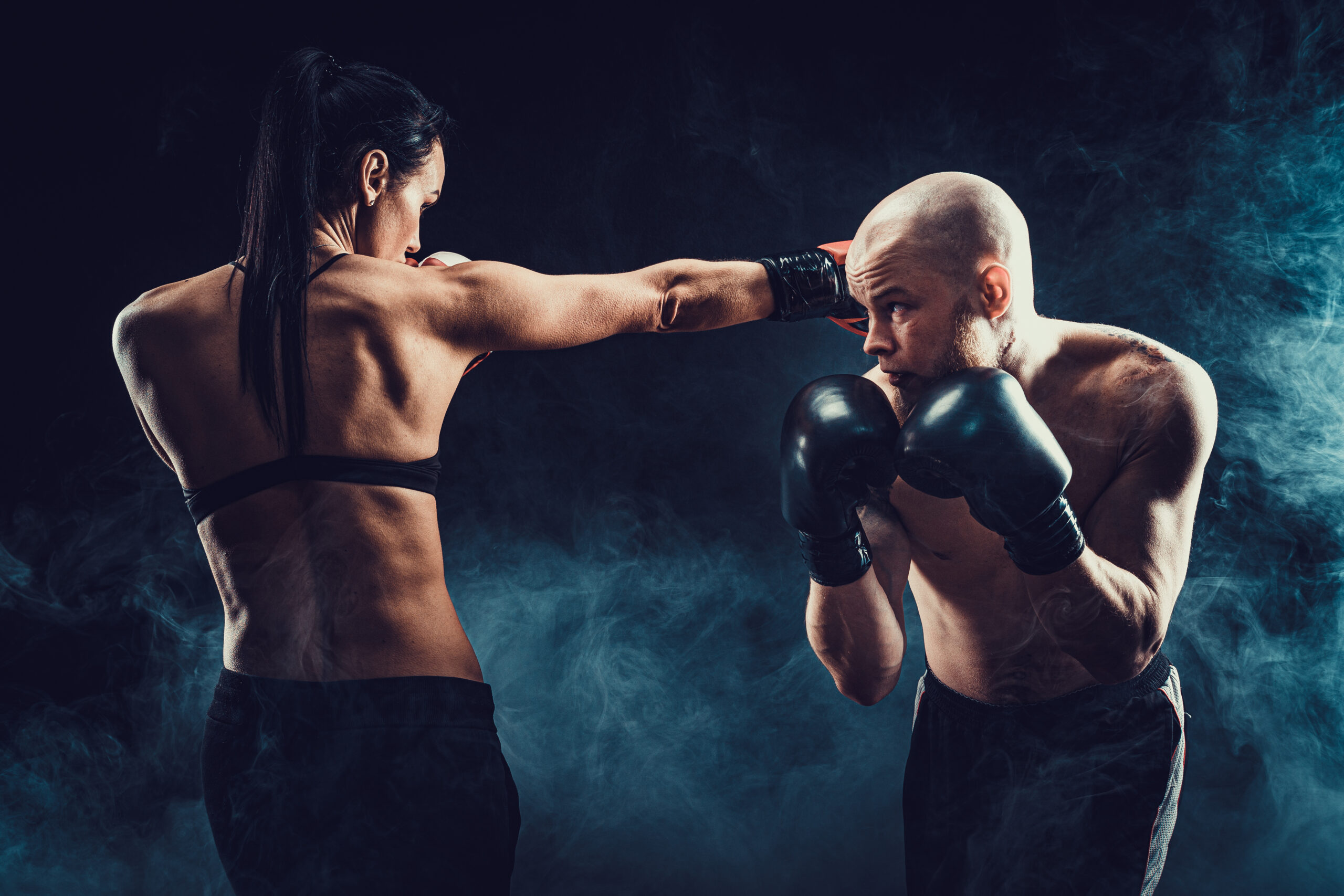 Shirtless Woman exercising with trainer at boxing and self defense lesson, studio, smoke on background